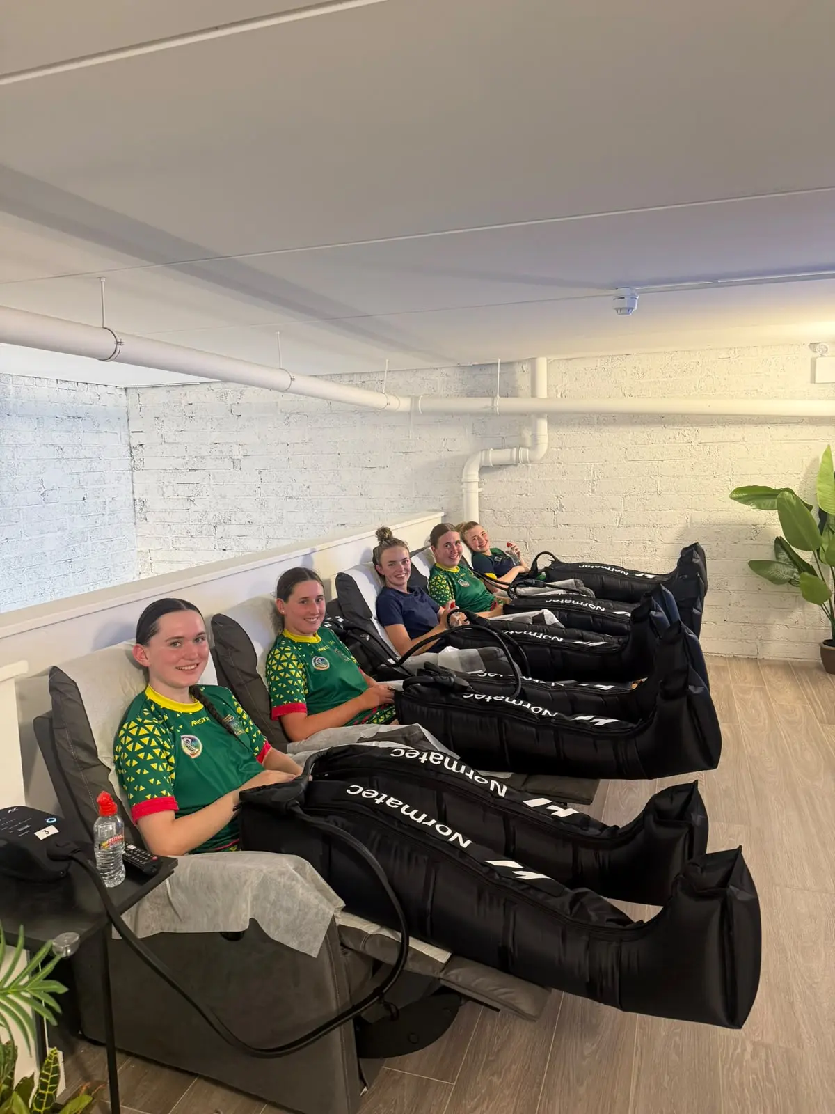 Guests in the compression lounge, the row of recliners seen from the door, plants in the corner