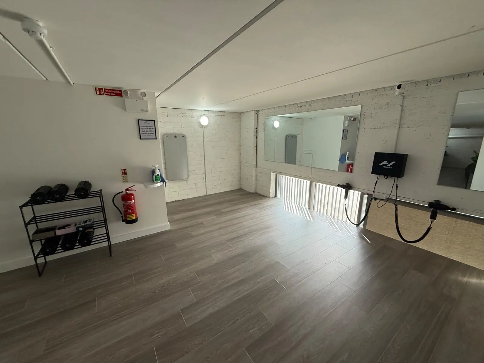 The empty mobility floor: foam rollers on a rack by the door, the mirrors and the massage guns on the far wall