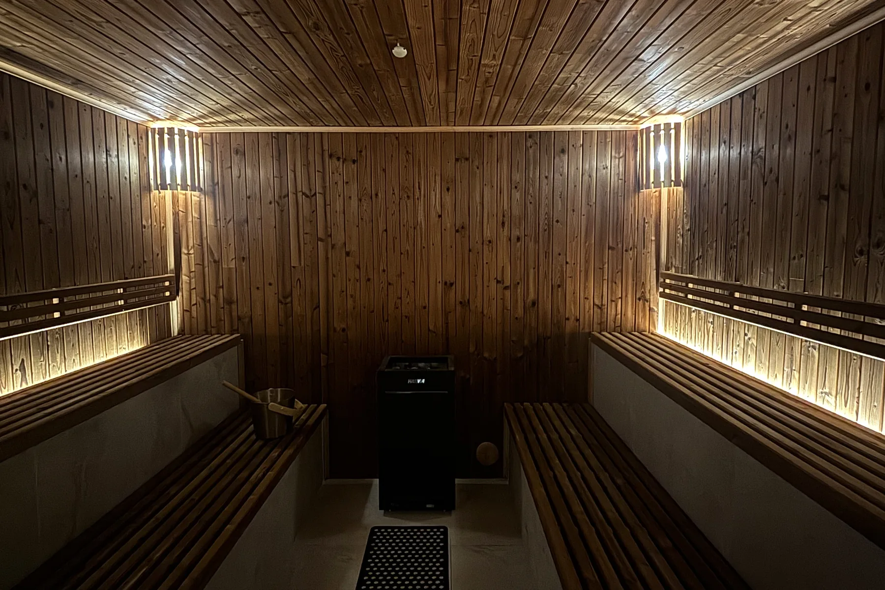 The sauna: pine-clad walls and ceiling, slatted benches down both sides lit from beneath, the heater at the far end